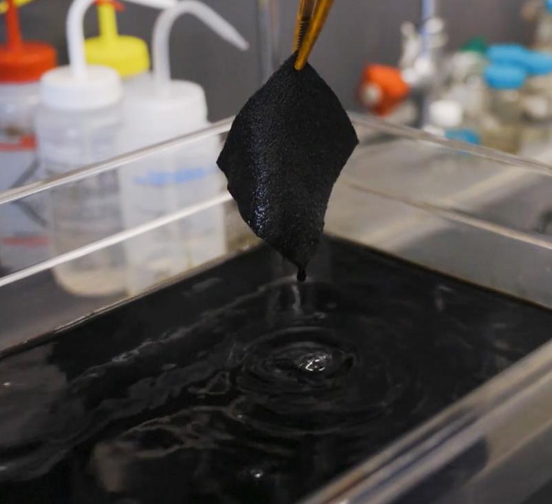 A person pulls a swatch of fabric out of ultrablack dye