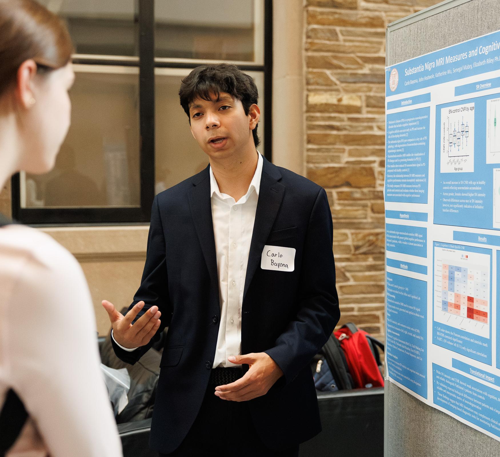 A student discusses their research with a poster next to them.