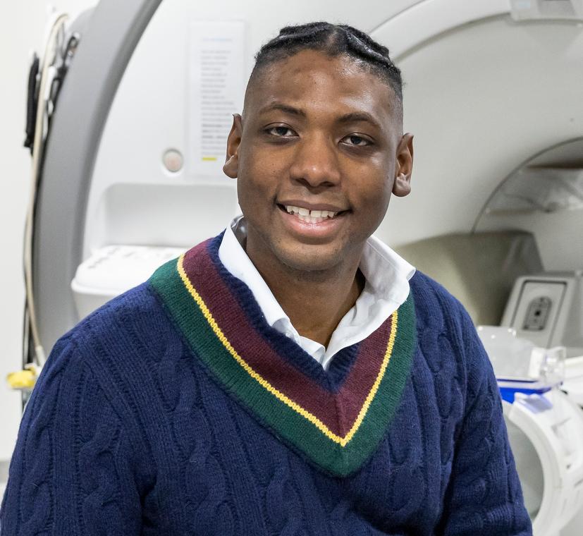 man in a blue sweater sitting on the bed of an MRI machine