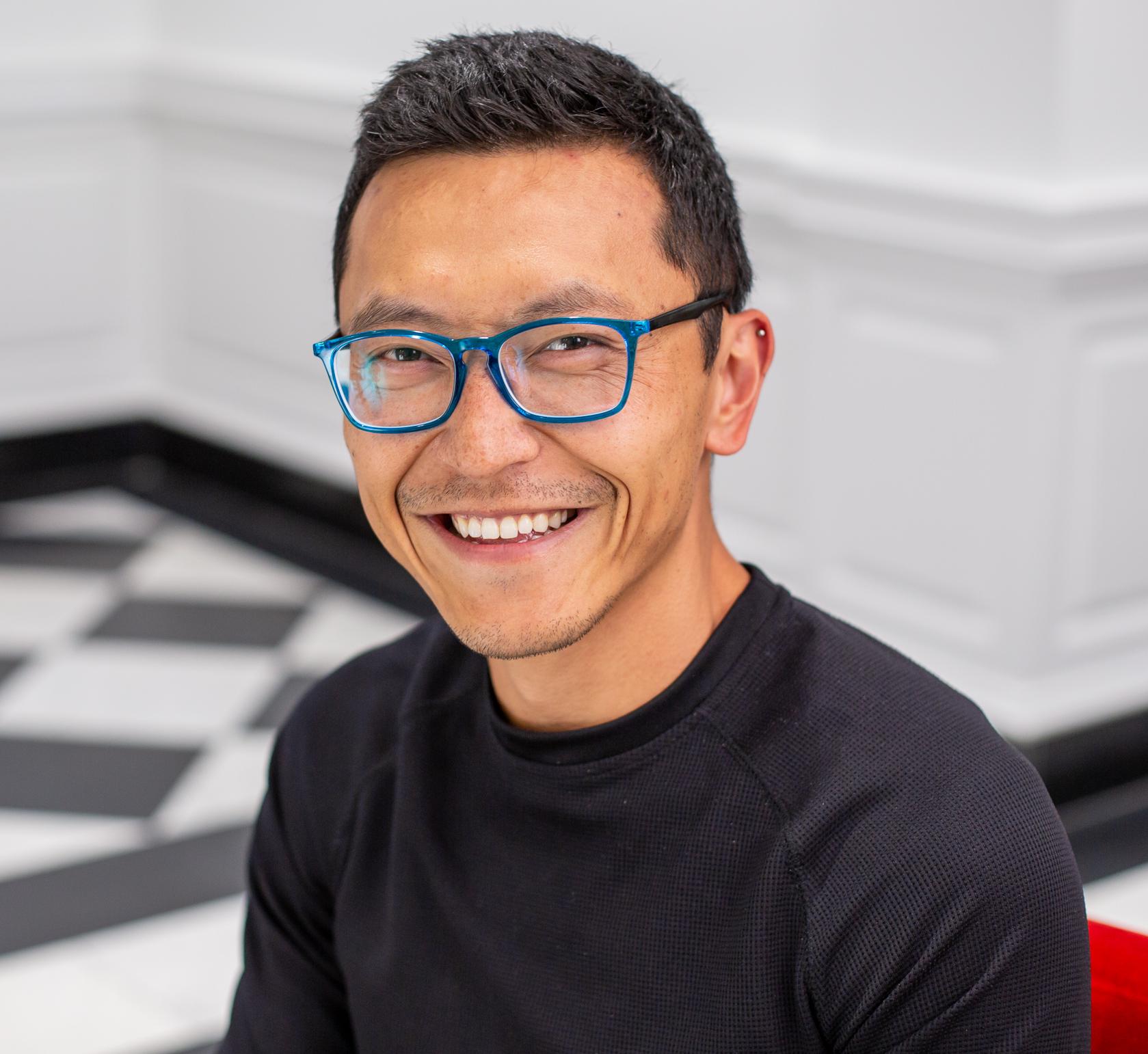 man in blue glasses sitting in a red chair and smiling