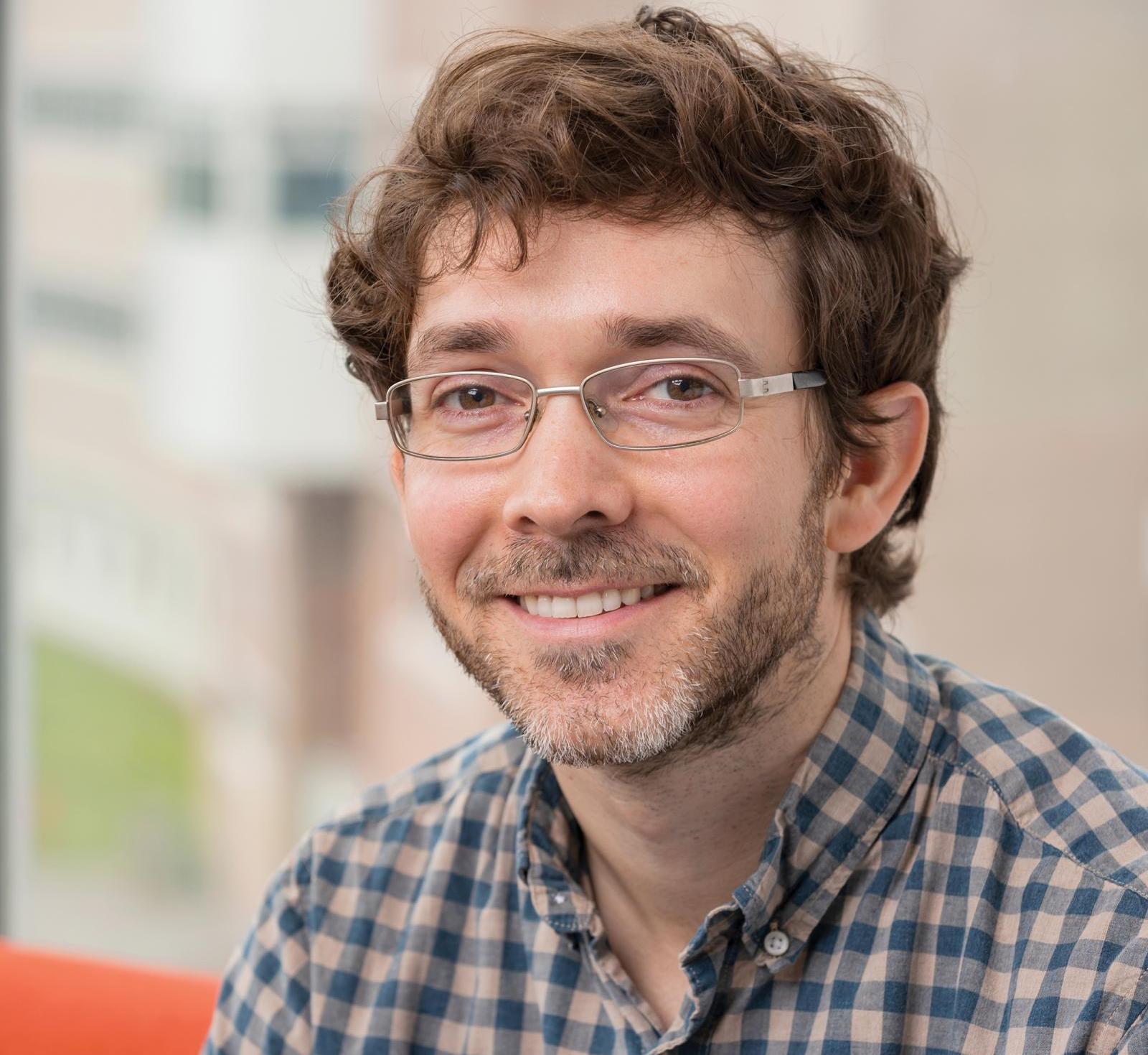 man in a plaid shirt smiling at the camera