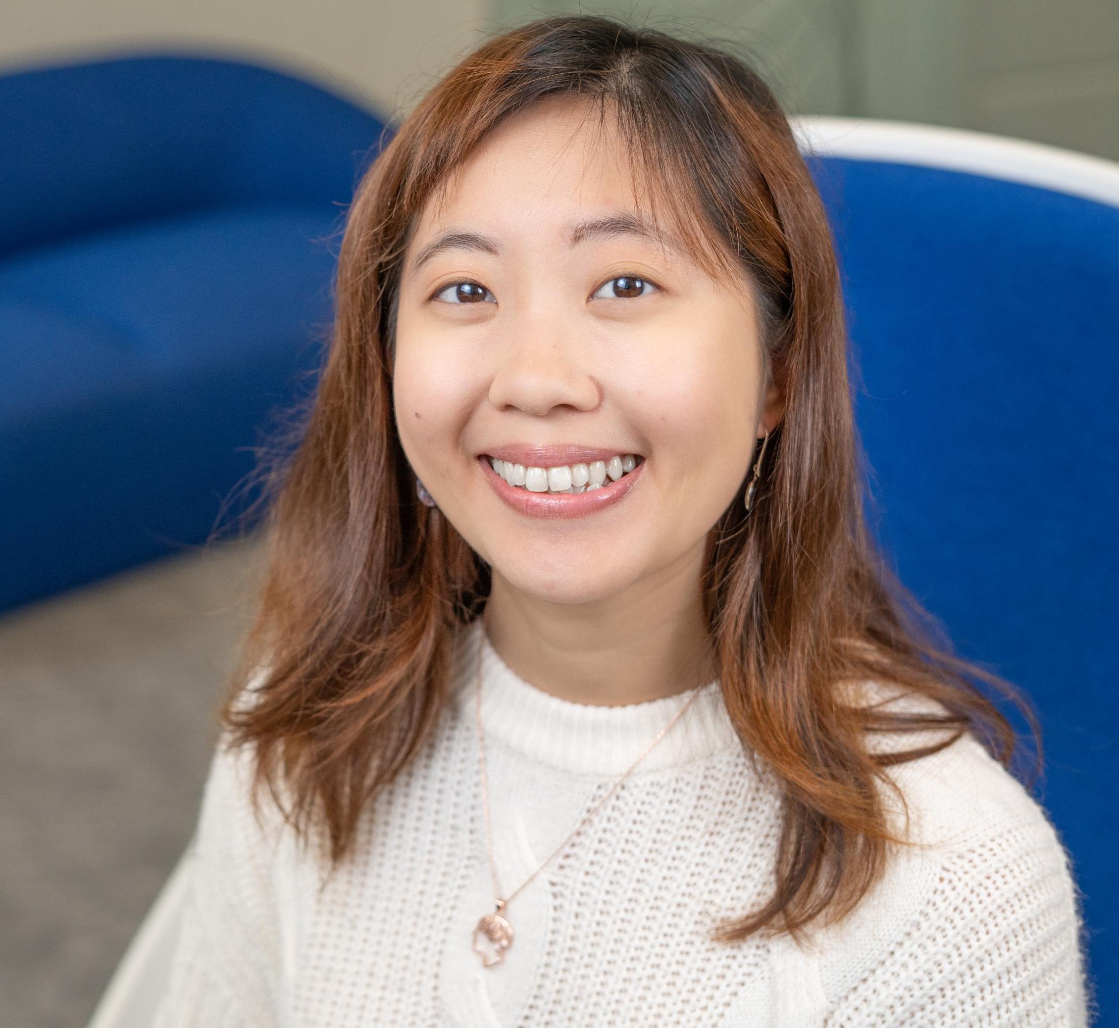 smiling person in white top sits in a bright blue chair