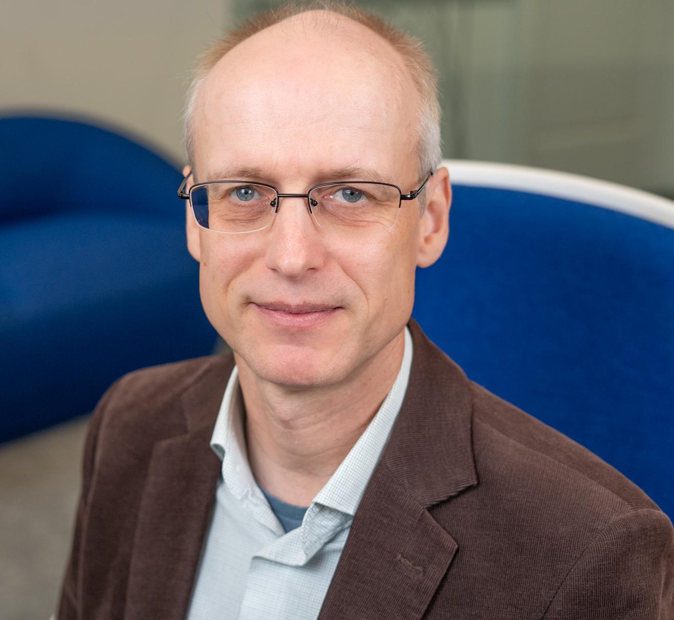 man in a brown blazer sitting in a bright blue chair