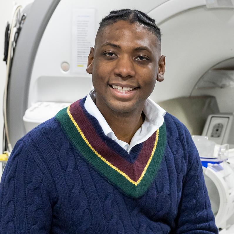 man in a blue sweater sitting on the bed of an MRI machine