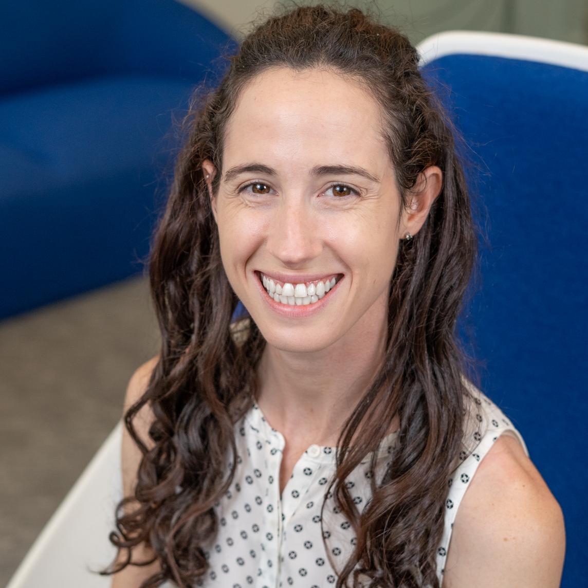 smiling woman with long brown hair sitting in a bright blue chair