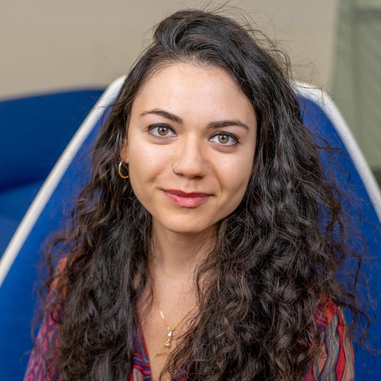 woman with long curly brown hair sitting in a bright blue chair