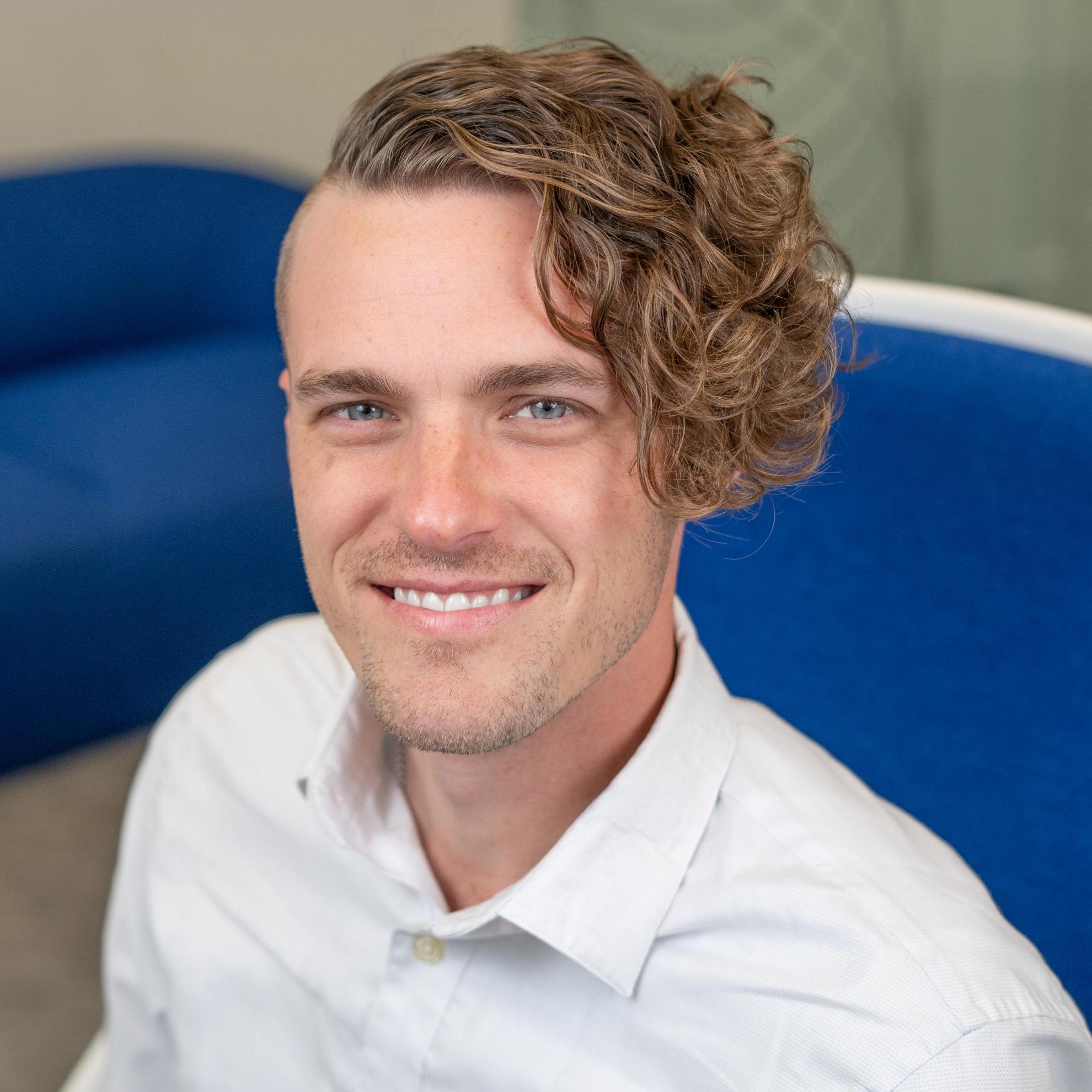 person with assymetrical curly hair sitting in a bright blue chair
