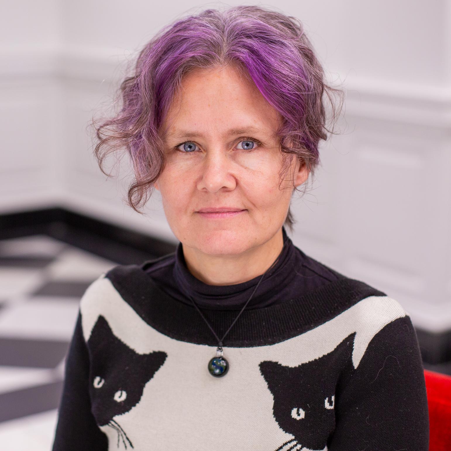 woman with purple hair wearing a sweater with black cats on it