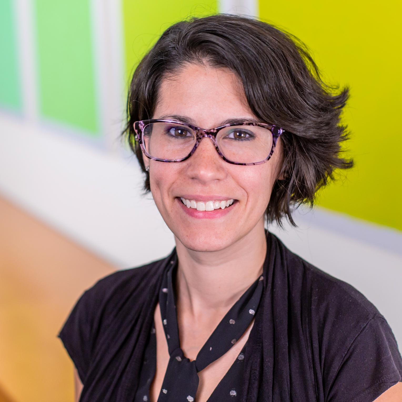 portrait of a woman wearing glasses and standing in front of bright green panels