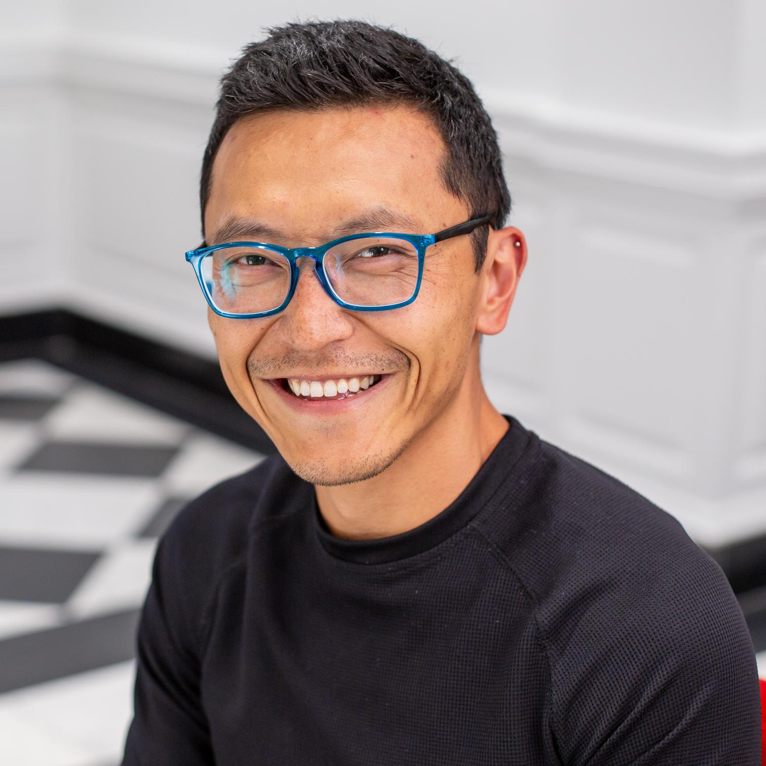 man in blue glasses sitting in a red chair and smiling