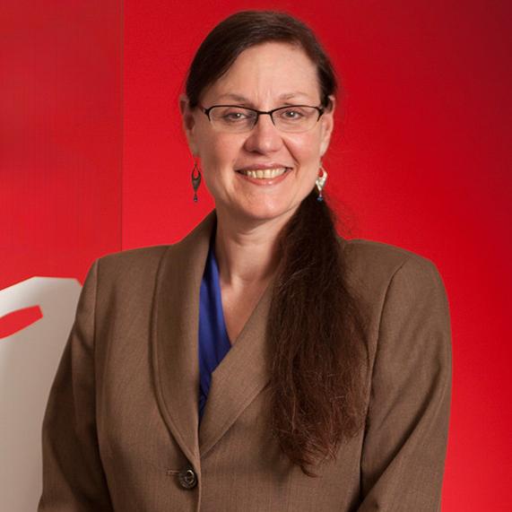 woman wearing a brown blazer standing in front of a red wall