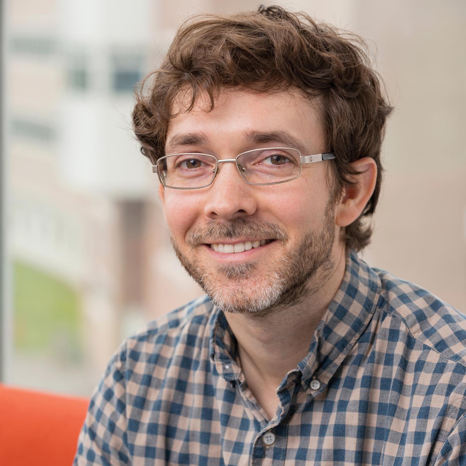 man in a plaid shirt smiling at the camera