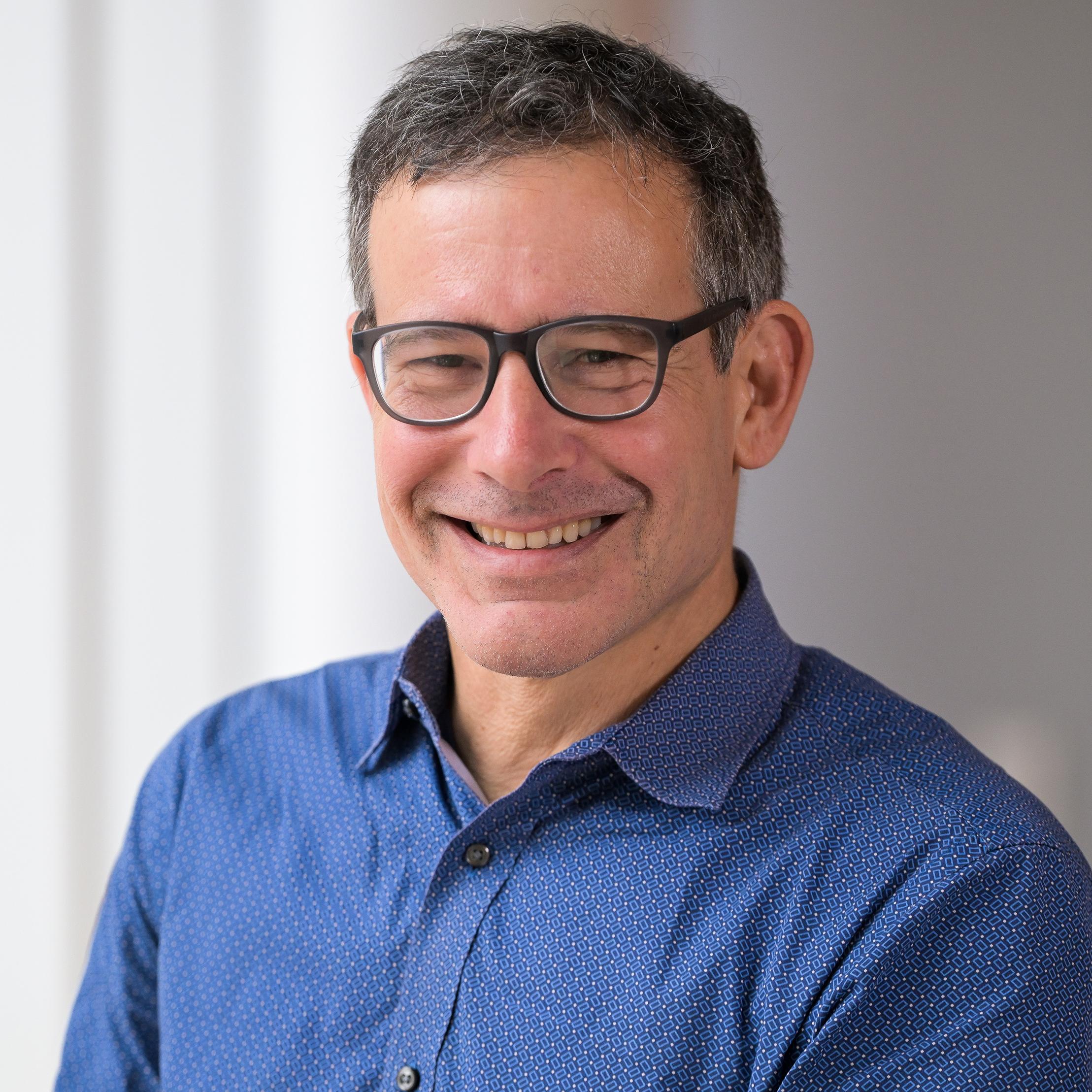 man with glasses wearing a blue shirt smiling at the camera