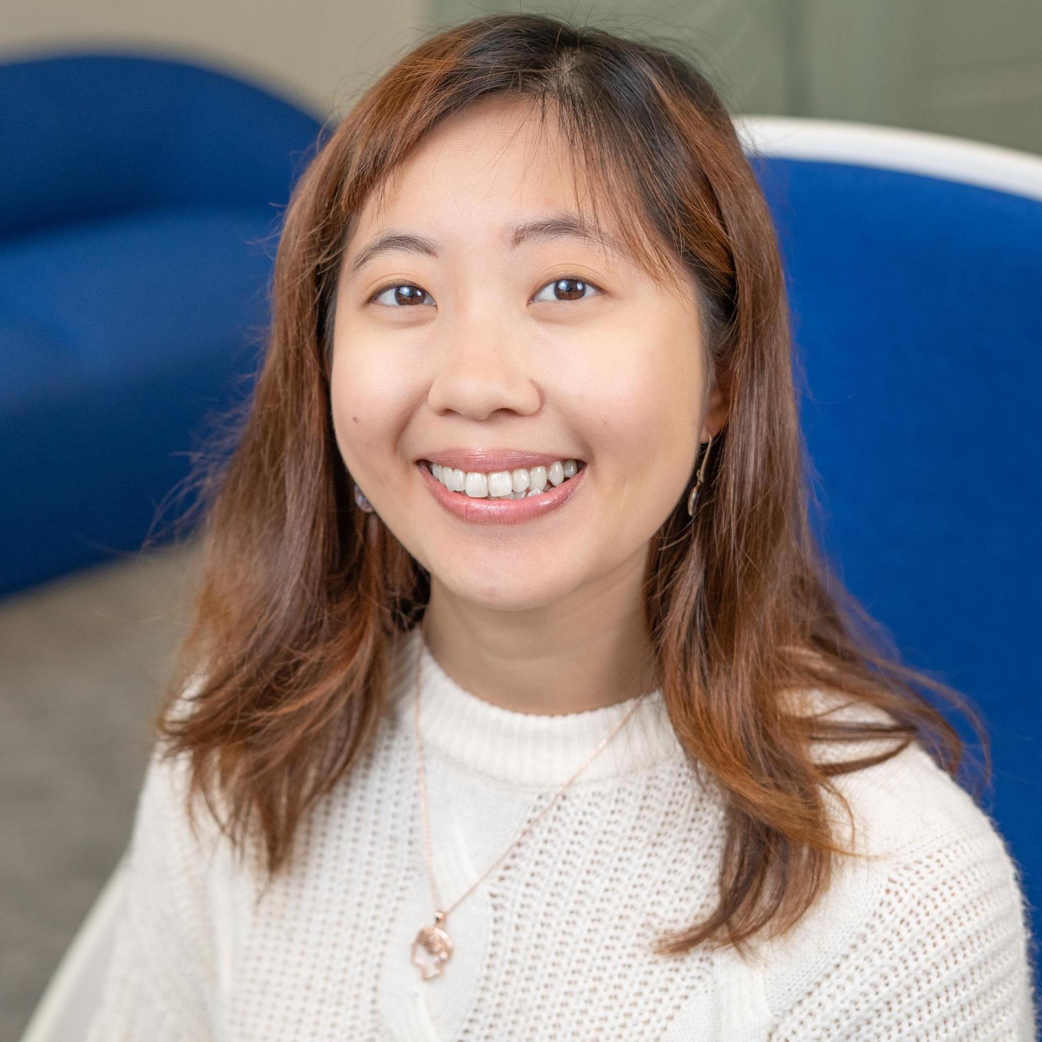 smiling person in white top sits in a bright blue chair