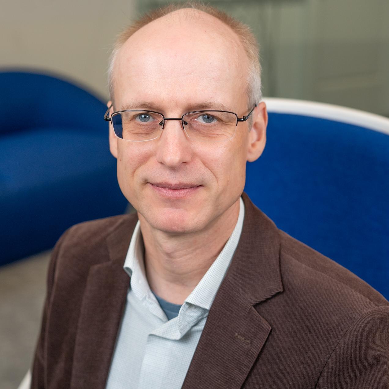 man in a brown blazer sitting in a bright blue chair