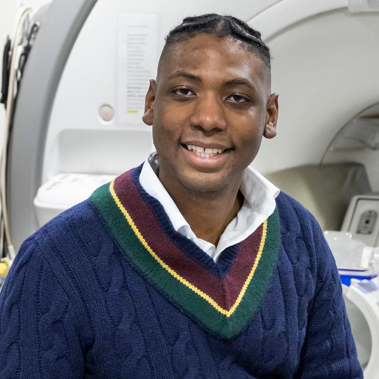 man in a blue sweater sitting on the bed of an MRI machine