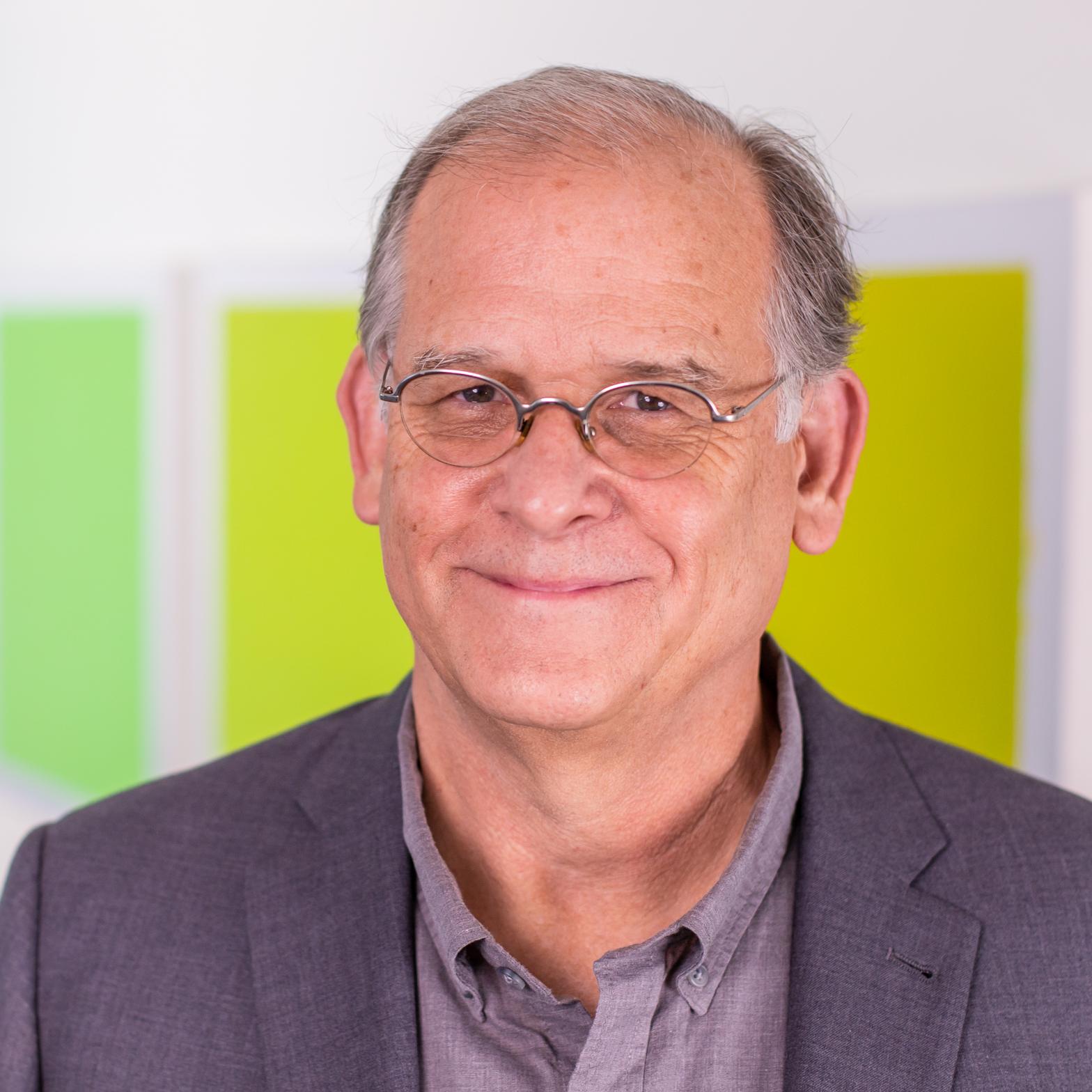 man in a grey suit standing in front of bright green panels