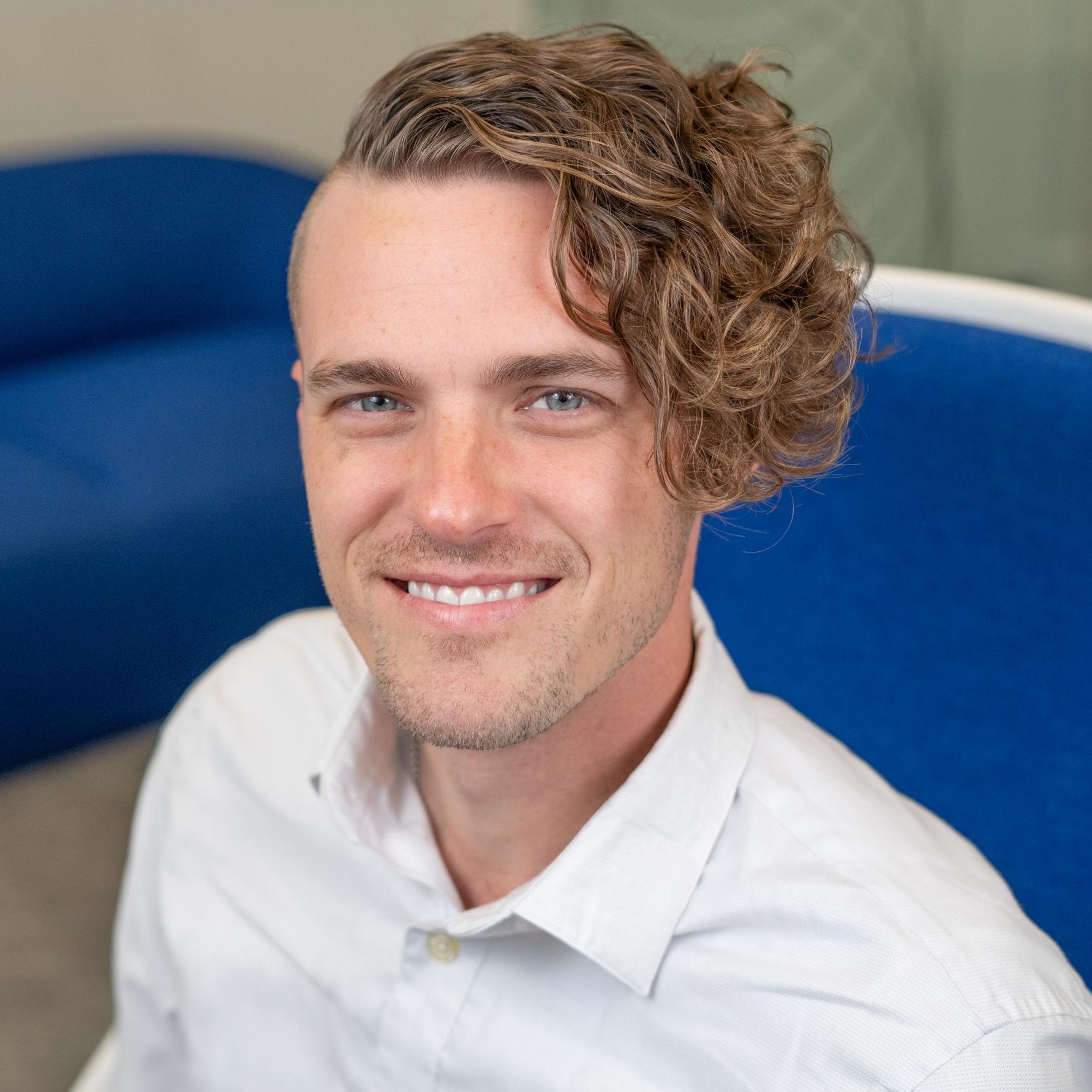person with assymetrical curly hair sitting in a bright blue chair
