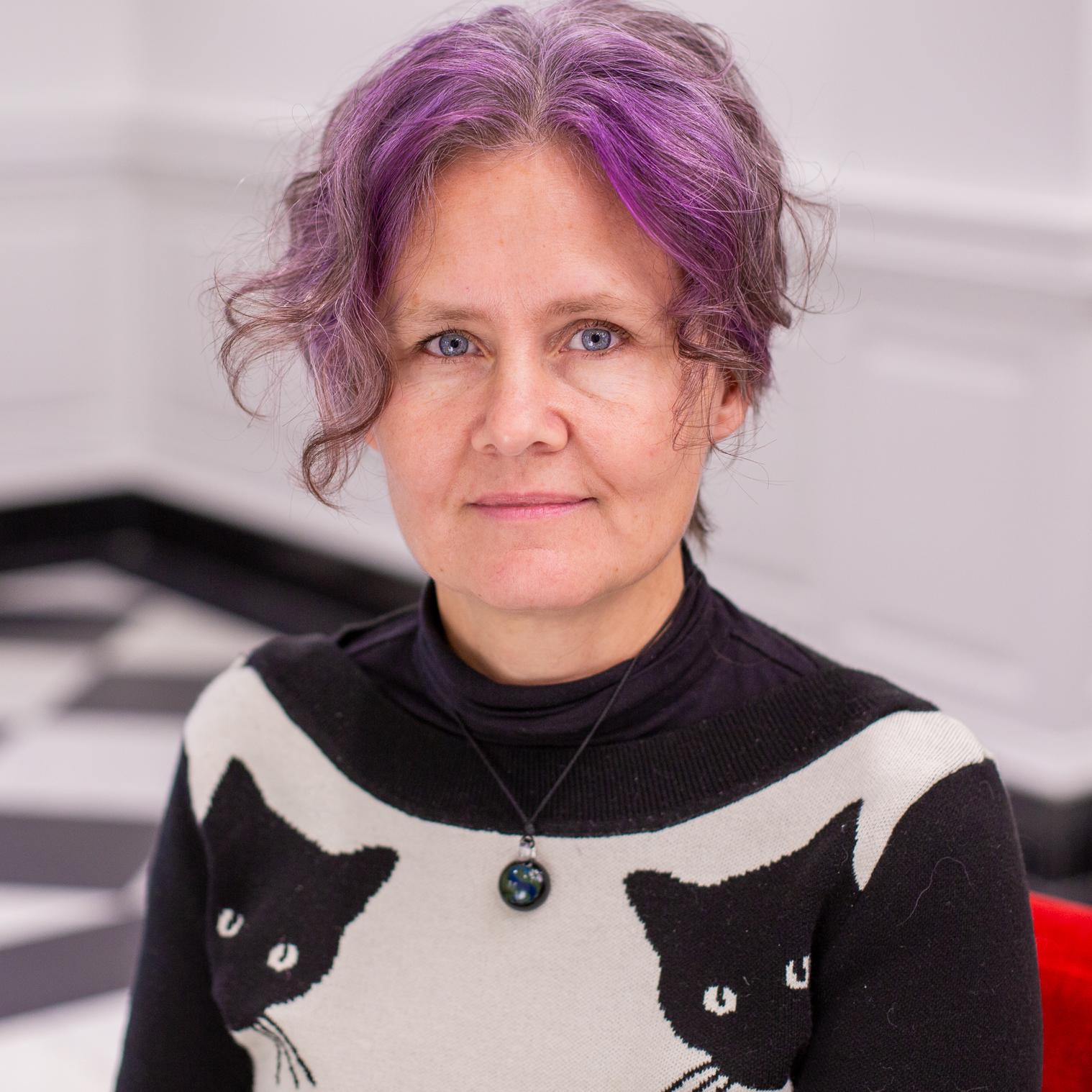 woman with purple hair wearing a sweater with black cats on it