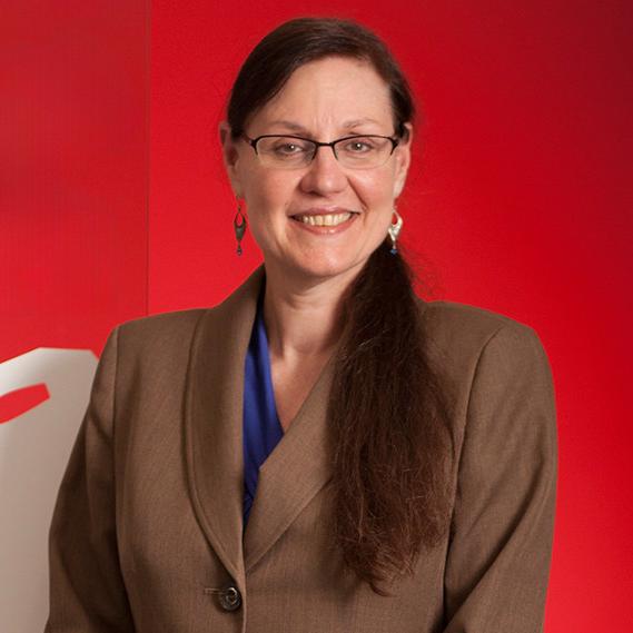 woman wearing a brown blazer standing in front of a red wall