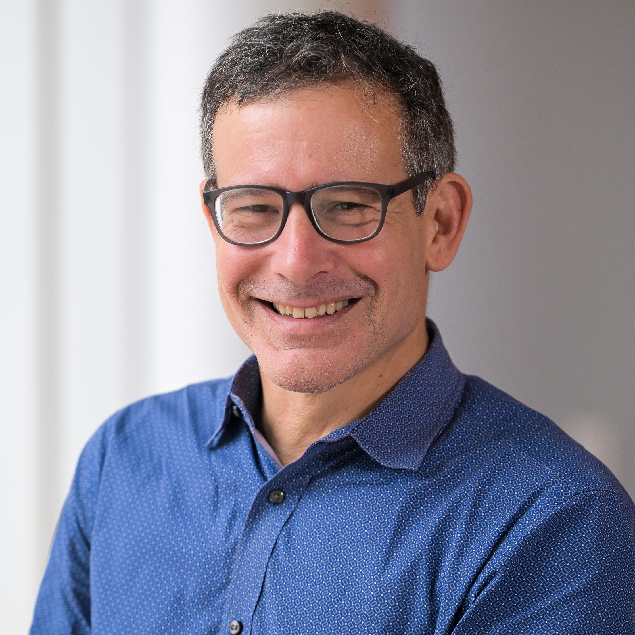 man with glasses wearing a blue shirt smiling at the camera
