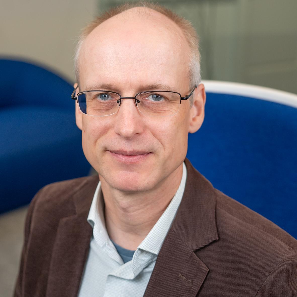 man in a brown blazer sitting in a bright blue chair