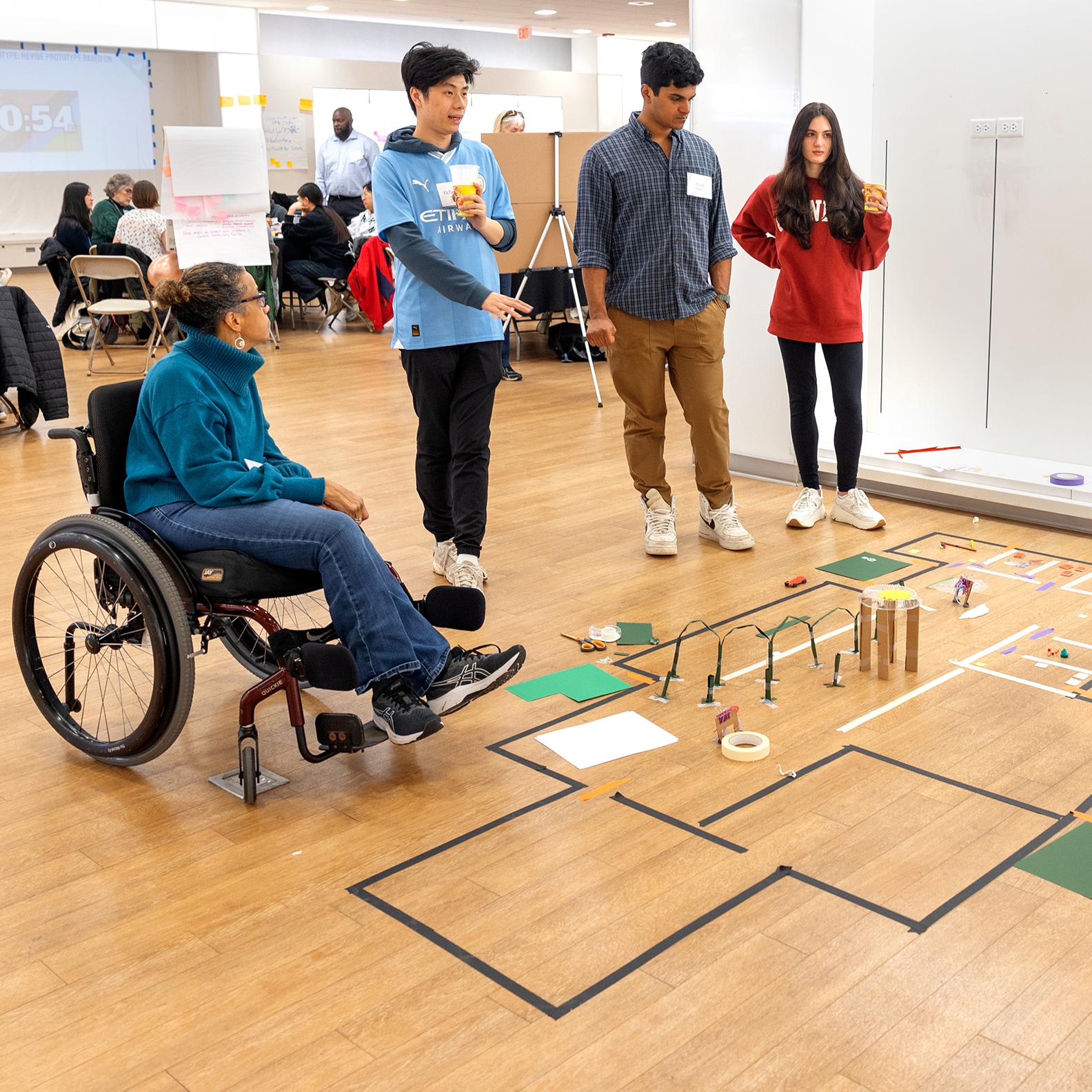 group of people standing around a model of a floorplan on the ground
