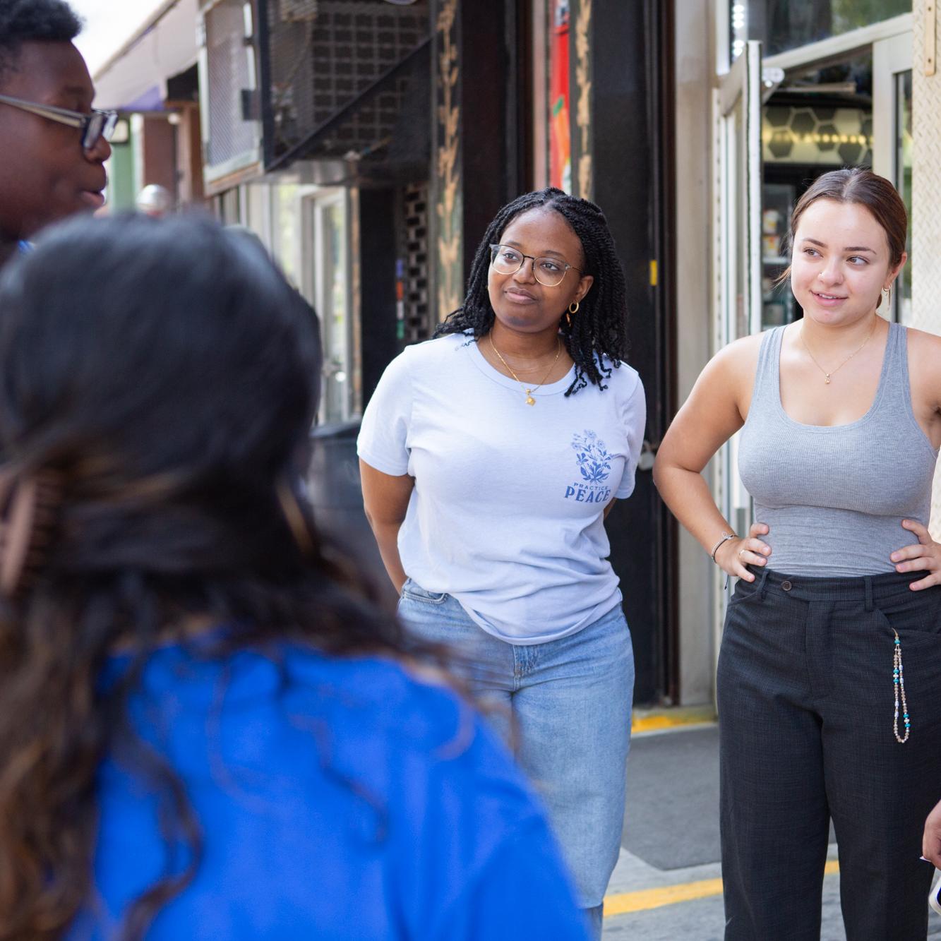 undergrad students talking to youth in blue t-shirts on the sidewalk outside a deli in NYC