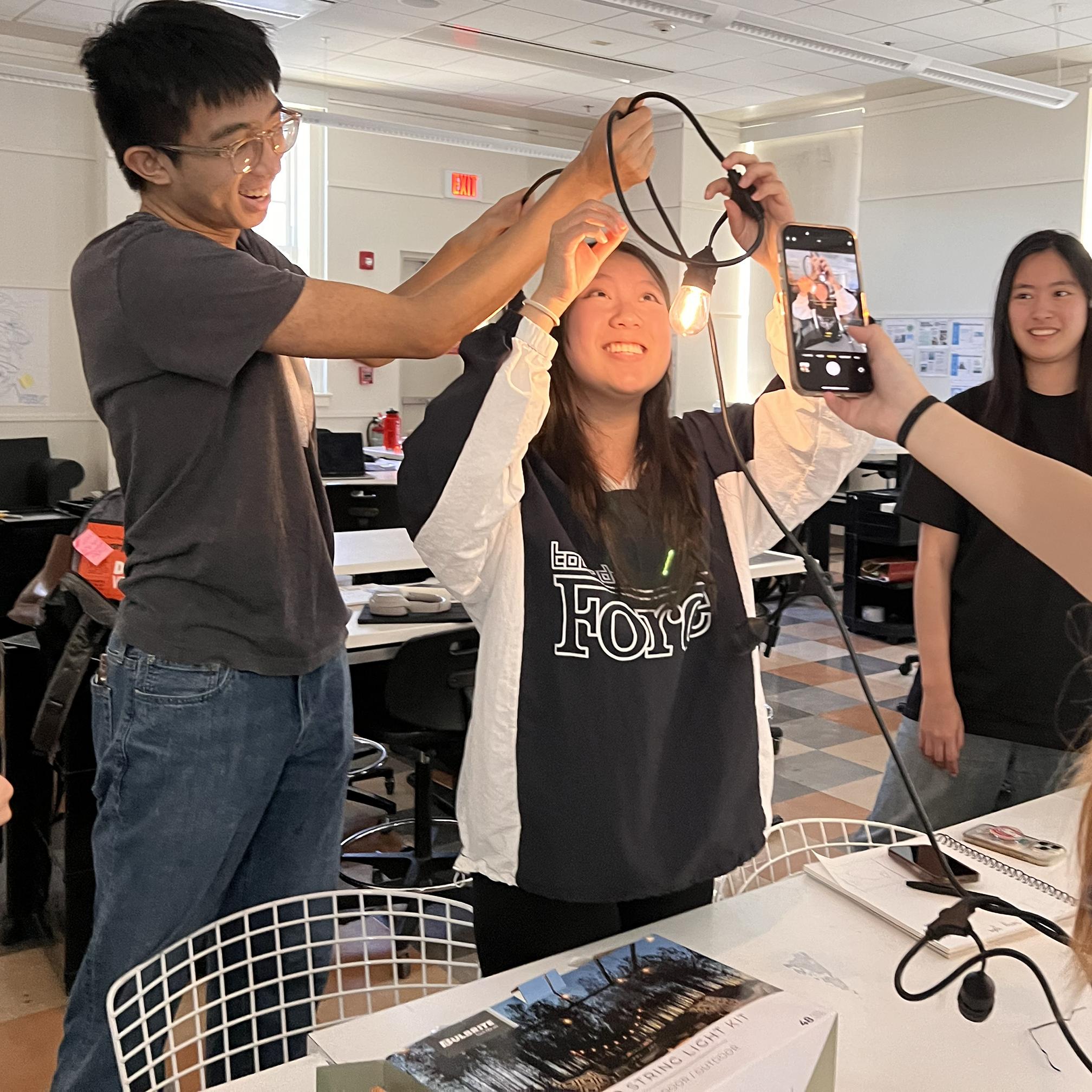 students holding up string lights in a classroom