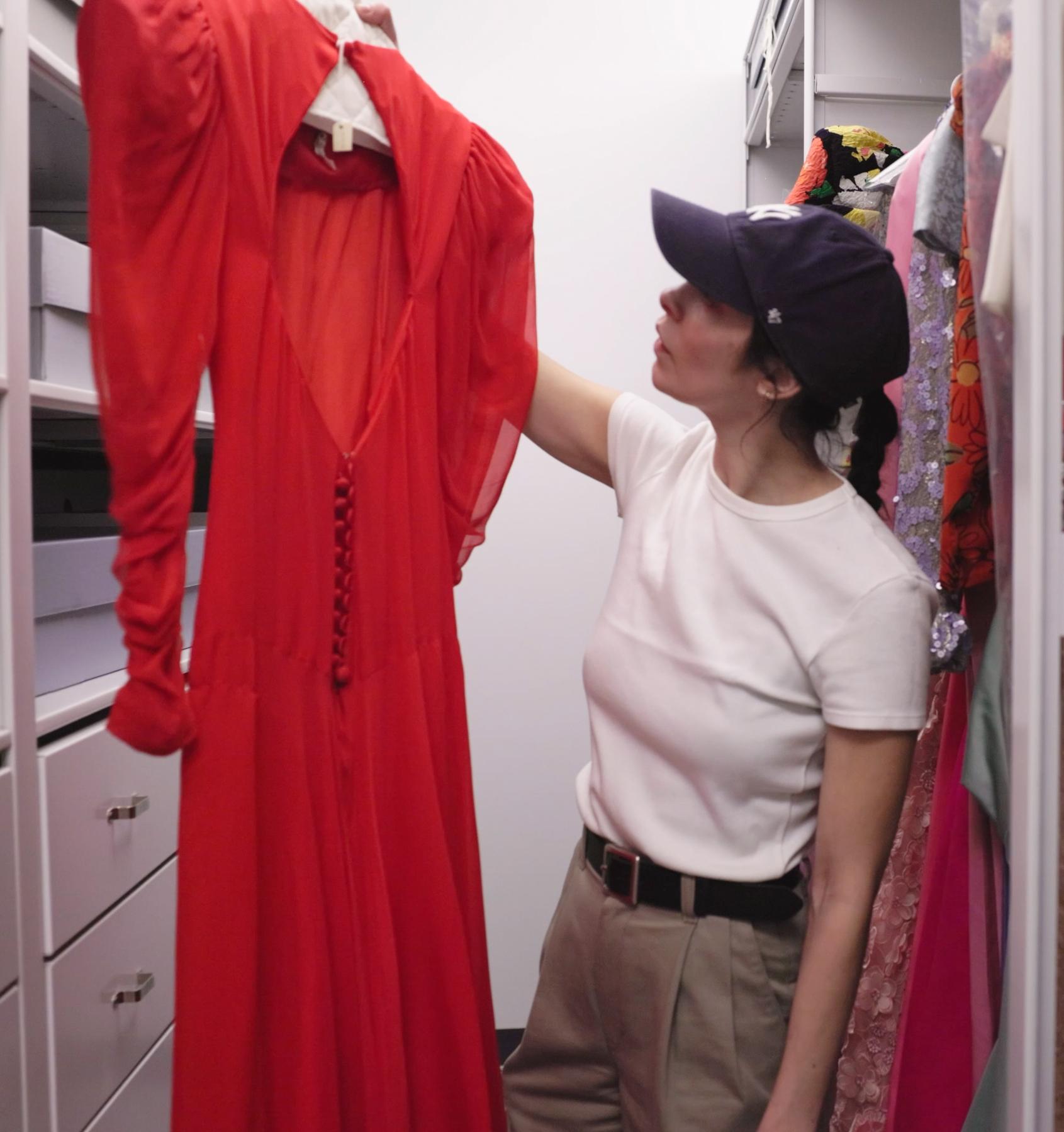 student holding up a vintage red dress on a hanger