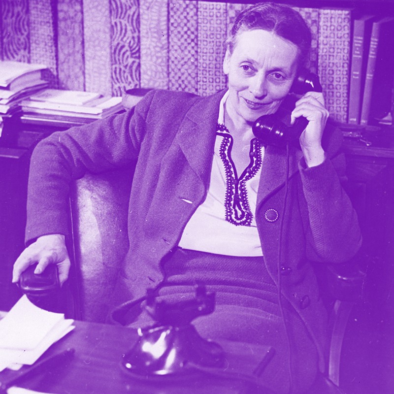 1941 black and white photo with purple tint showing a woman seated at a desk talking on a telephone