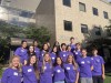 18 DNS student peer advisors pose together in matching shirts in front of Savage/Kinzelberg Hall in the sun.